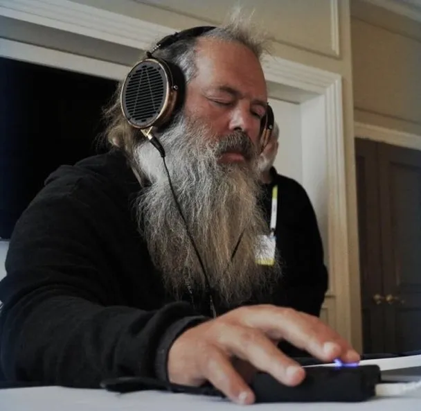 A bearded man is working on his laptop while listening to music with headphones.